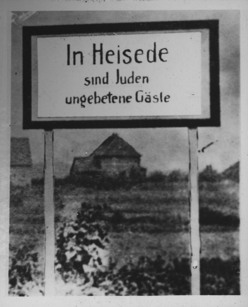 Sign in front of a field with houses in the background.