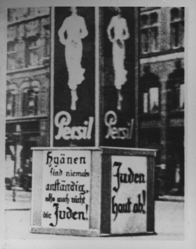 Anti-Semitic posters written in German on a billboard in the middle of a street. 