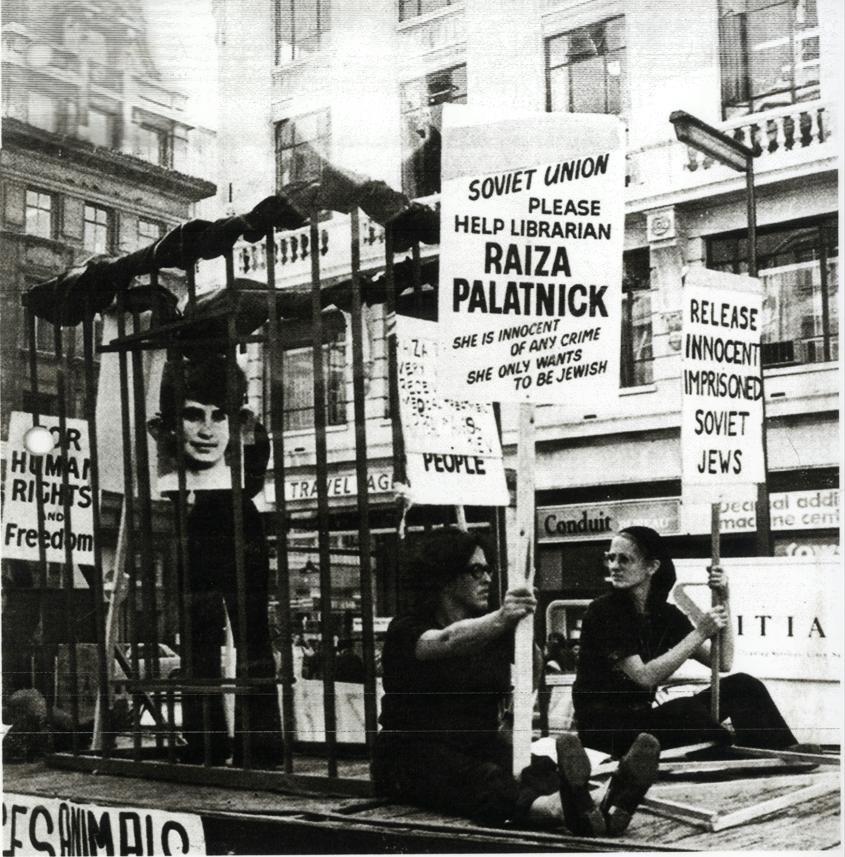 Two women protesting, holding signs and sitting on a float in the middle of a street.