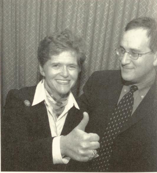 Black and white photograph of a man and a woman with her thumb up wearing suits.