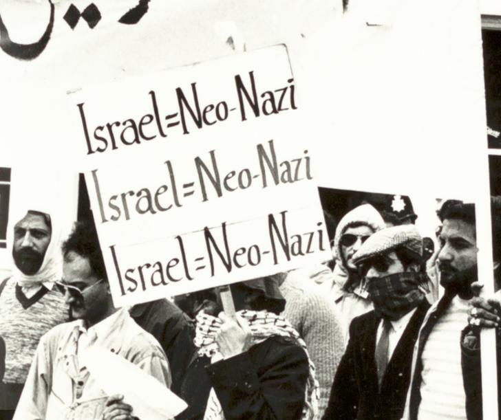 crowd of men holding up banners. In the centre of the photograph a man is holding a sign which reads 'Israel= Neo- Nazi'.