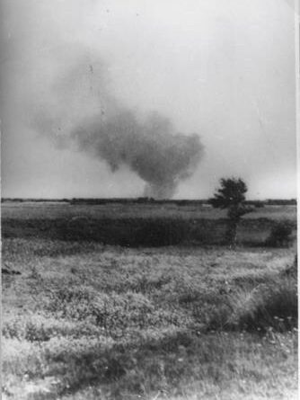 Black and white photograph of a field with smoke in the distance.